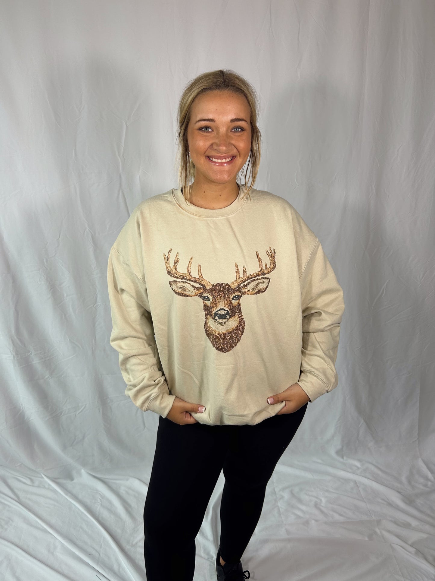 Person wearing a beige sweatshirt with a deer graphic on a plain background